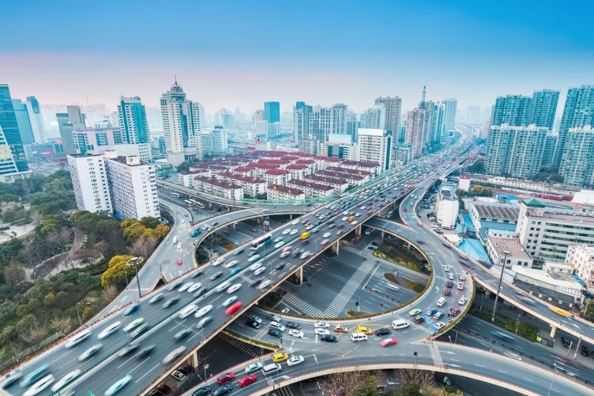 sprimontblue Vue aérienne d'un échangeur routier complexe dans une ville dense, mettant en valeur l'infrastructure urbaine et la circulation.