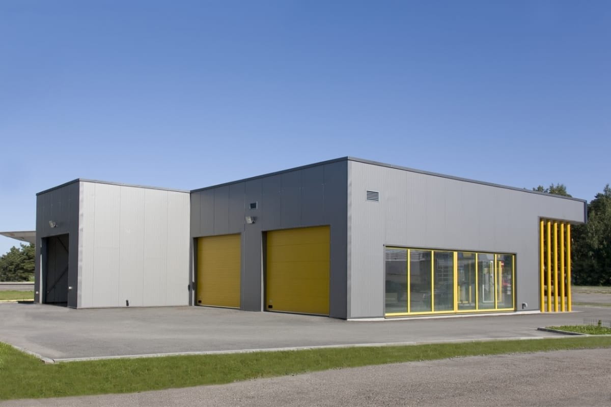 sprimontblue Bâtiment commercial gris moderne avec portes enroulables jaunes et grandes fenêtres.