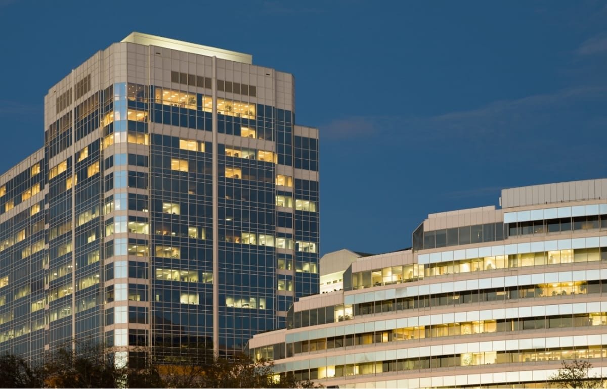 sprimontblue Deux immeubles de bureaux modernes au crépuscule, fenêtres illuminées.