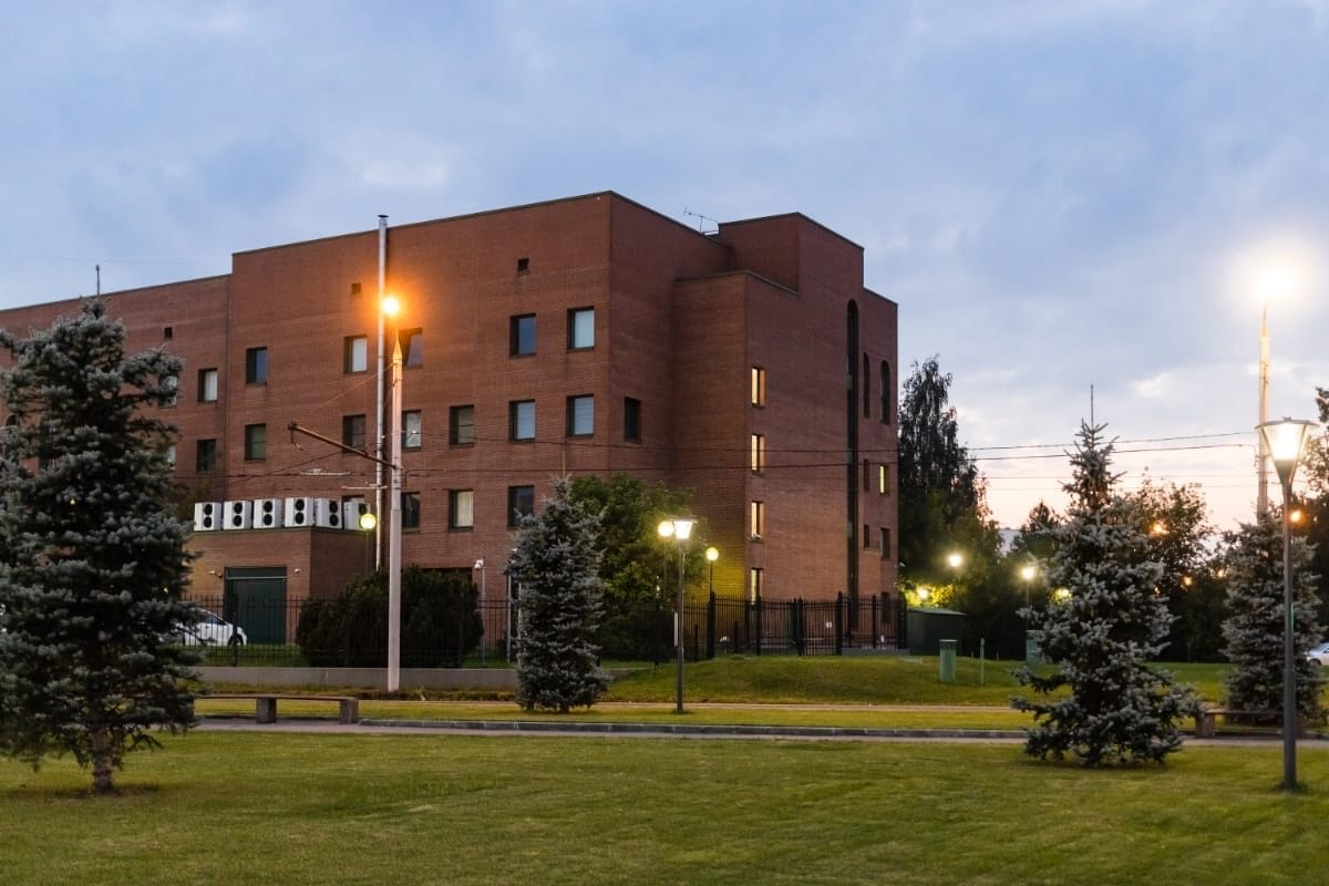 sprimontblue Bâtiment moderne en briques au crépuscule avec aménagement paysager et lampadaires.