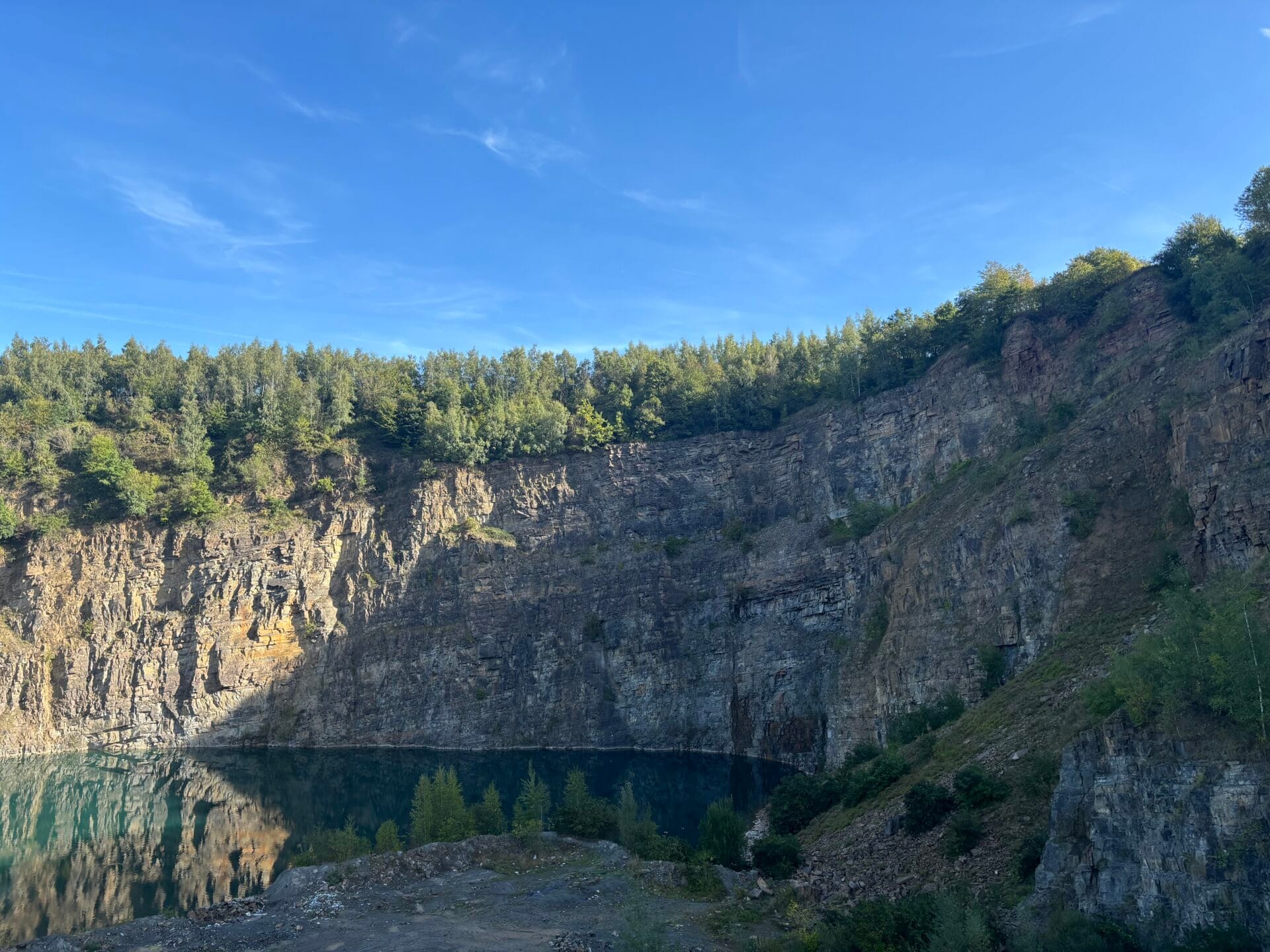 sprimontblue Carrière de grès belge avec lac et falaises de pierre naturelle sous un ciel bleu.